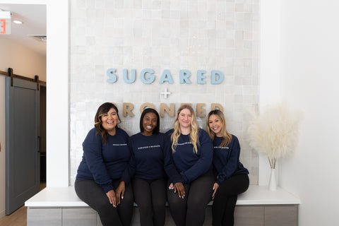 Four women in matching navy blue sweatshirts sitting in front of a 'Sugared & Rendered' sign.