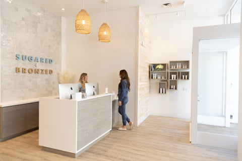Modern interior of a salon with reception desk and 'Sugared & Bronzed' sign.