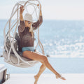 Woman sitting in a hanging chair by the ocean