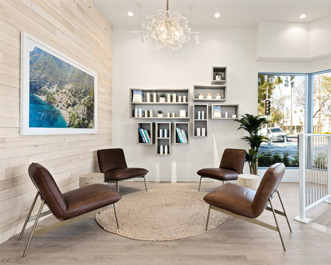Modern store waiting room with brown chairs, a round rug, and a bookshelf.