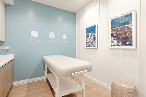 Treatment room with a massage table against a blue wall with 'sugar lemon water' text.