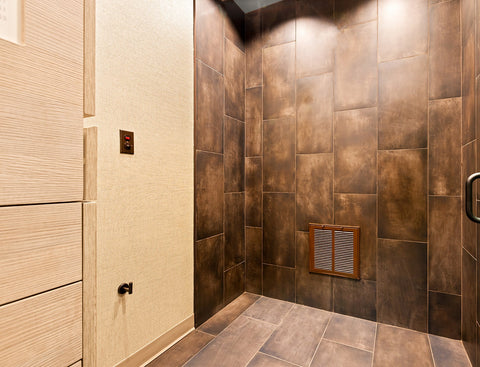 Tanning spray room with brown tiled walls and floor, featuring a spray area. 