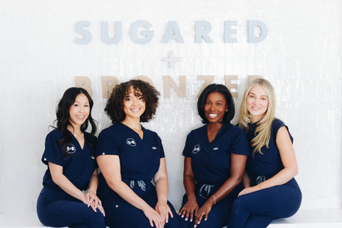 Team members in uniforms sitting in front of the Sugared + Bronzed logo