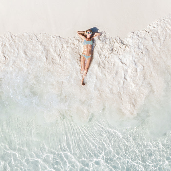 A woman in a bathing suit laying on her back on a sandy beach