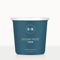A blue tub labeled 'SUGAR PASTE FIRM' from Sugared and Bronzed, containing sugar paste for hair removal.
