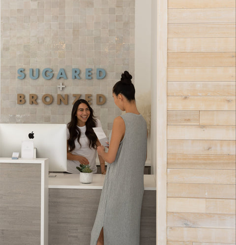 Woman receiving a service at a salon counter with 'Sugared + Bronzed' branding.