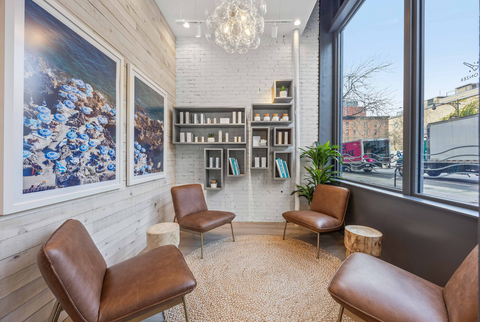 Modern interior lobby seating area with brown chairs, product shelves, and large windows.