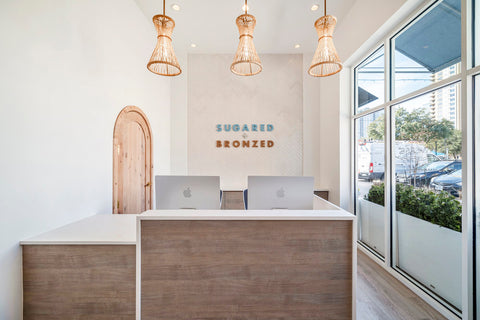 Lobby view of a reception desk with three pendant lights, glass windows and a tile wall with a logo sign on it