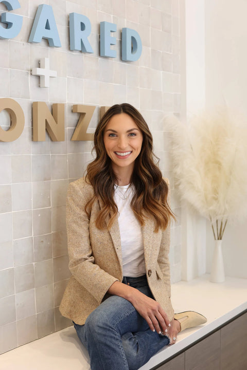 Courtney Claghorn, chairwoman and co-founder of `Sugared & Bronzed`, sitting and smiling in front of a wall containing the `Sugared & Bronzed` logo