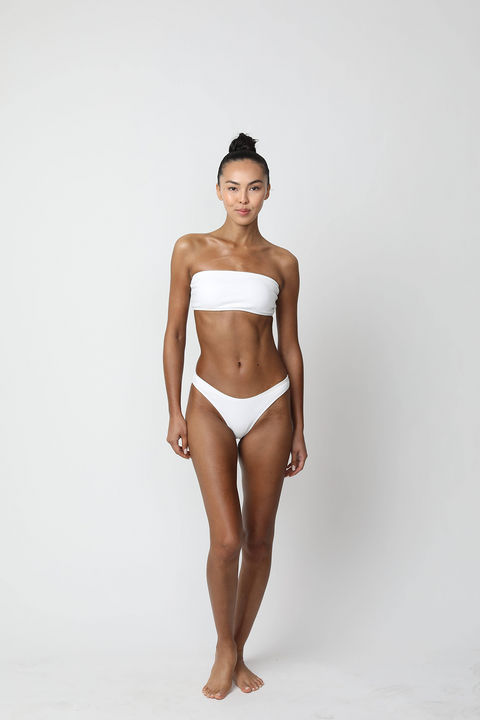 Woman with a tan wearing a white strapless bikini against a plain background