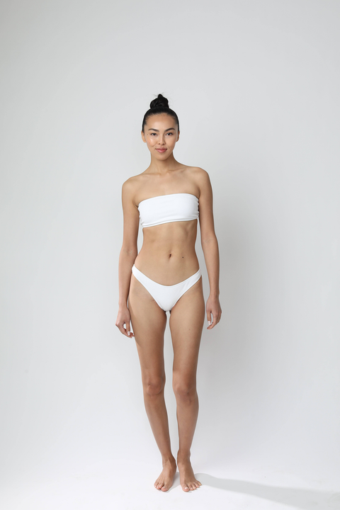 Woman without a tan wearing a white bikini on a plain background